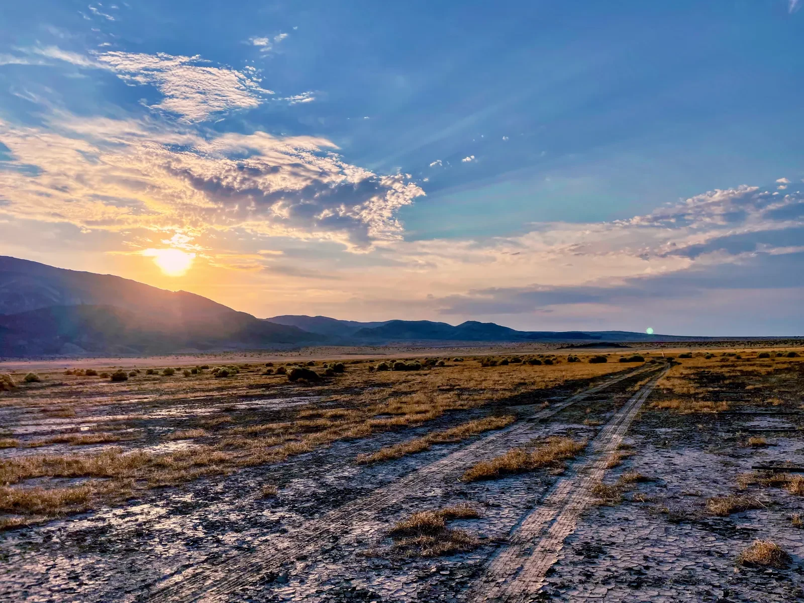 Desert tracks leading toward distant mountains under a glowing sunset sky near Landers, California.