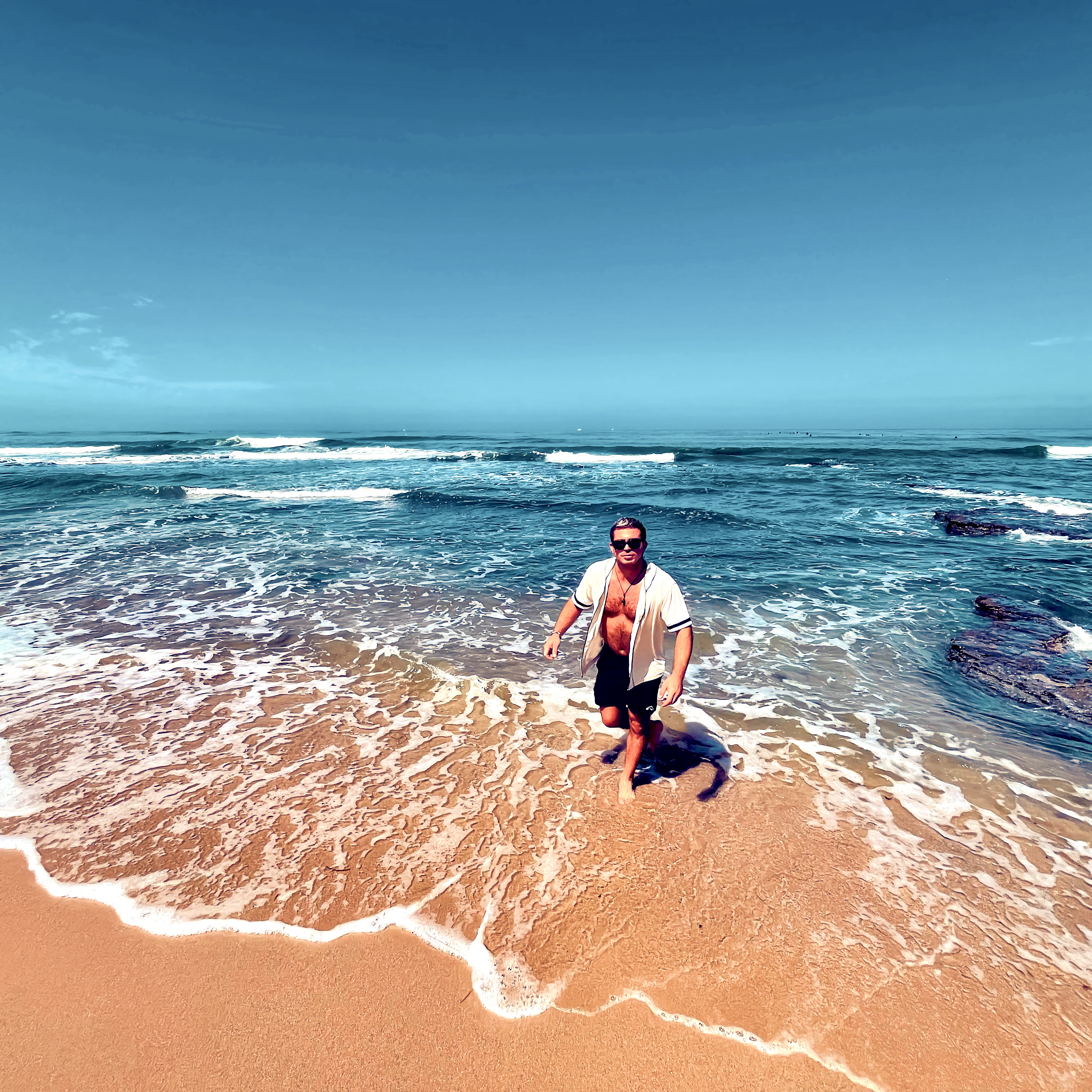 Walking through shallow ocean foam onto a sandy shore.