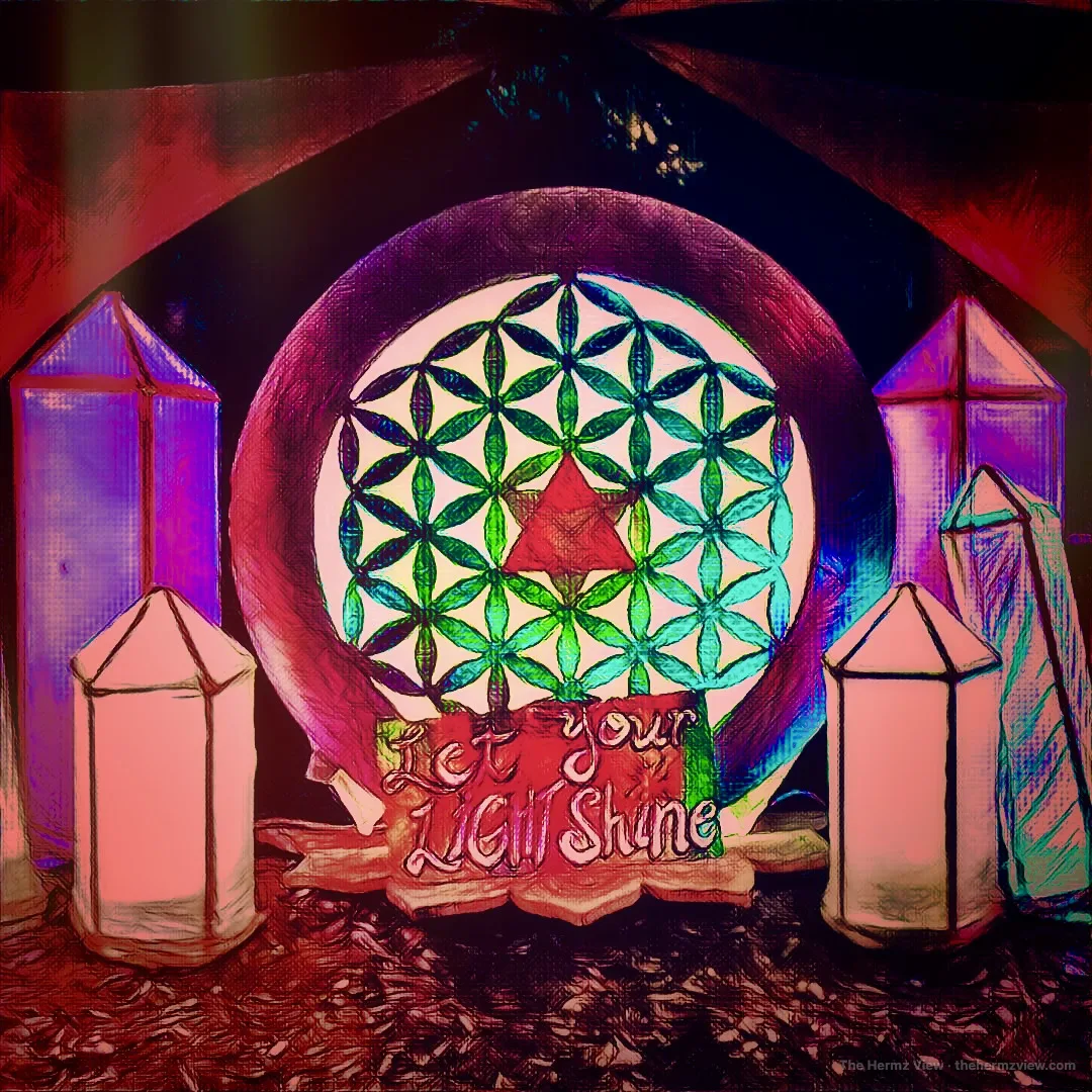 An illuminated art piece featuring glowing crystal pillars around a circular Flower of Life design with a sign that reads Let Your Light Shine.