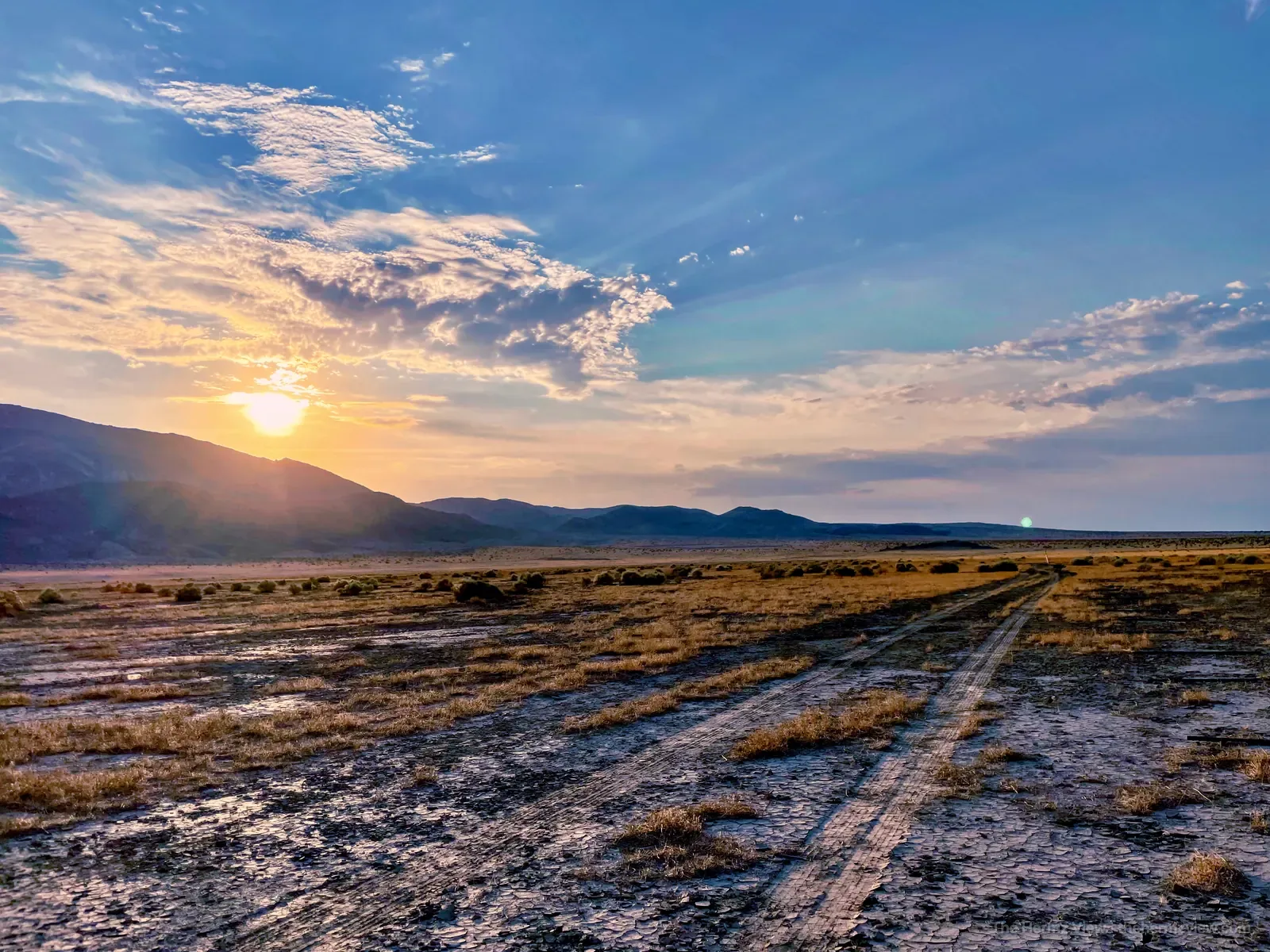 Desert tracks leading toward distant mountains under a glowing sunset sky near Landers, California.
