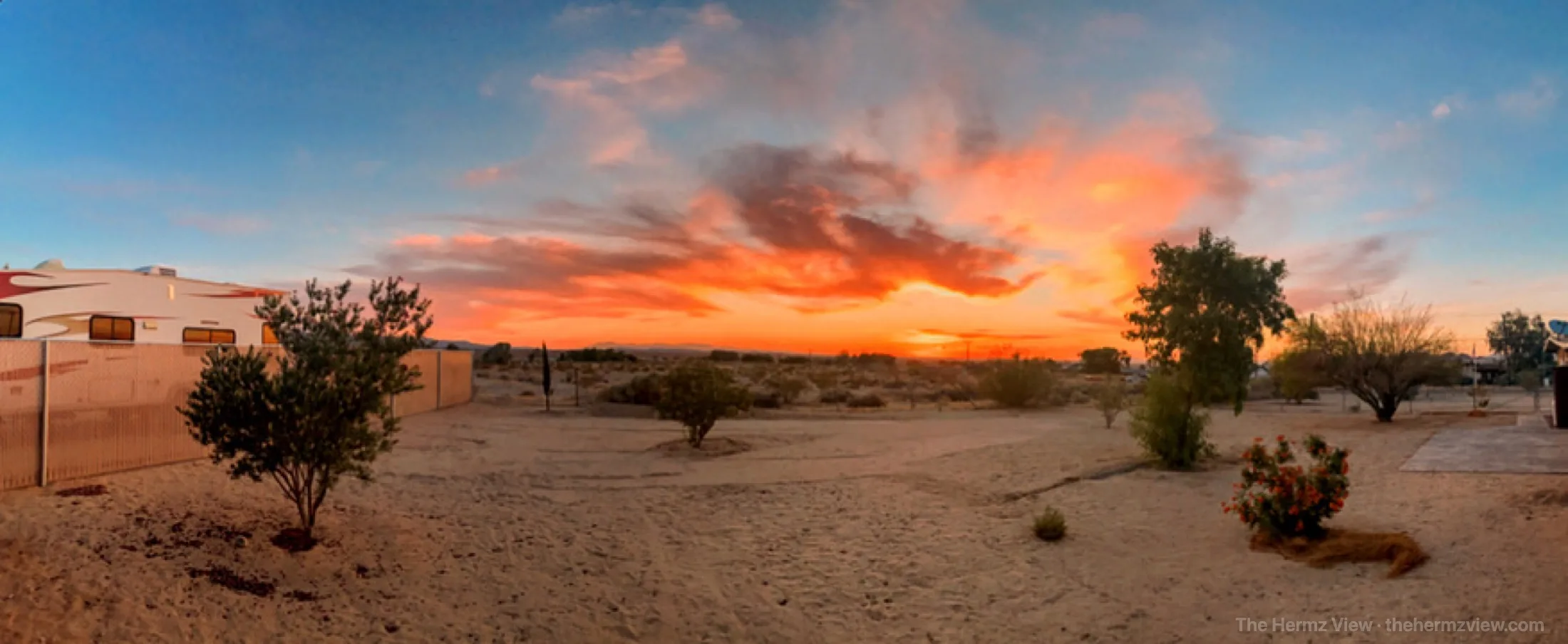 Desert camp glowing under a wide sunset