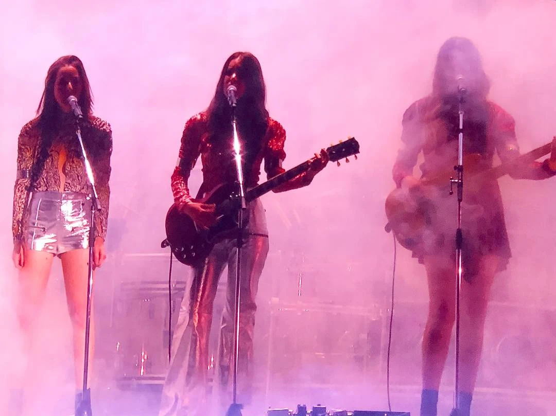 Three musicians on stage with guitars and microphones surrounded by dense pink fog and backlight.